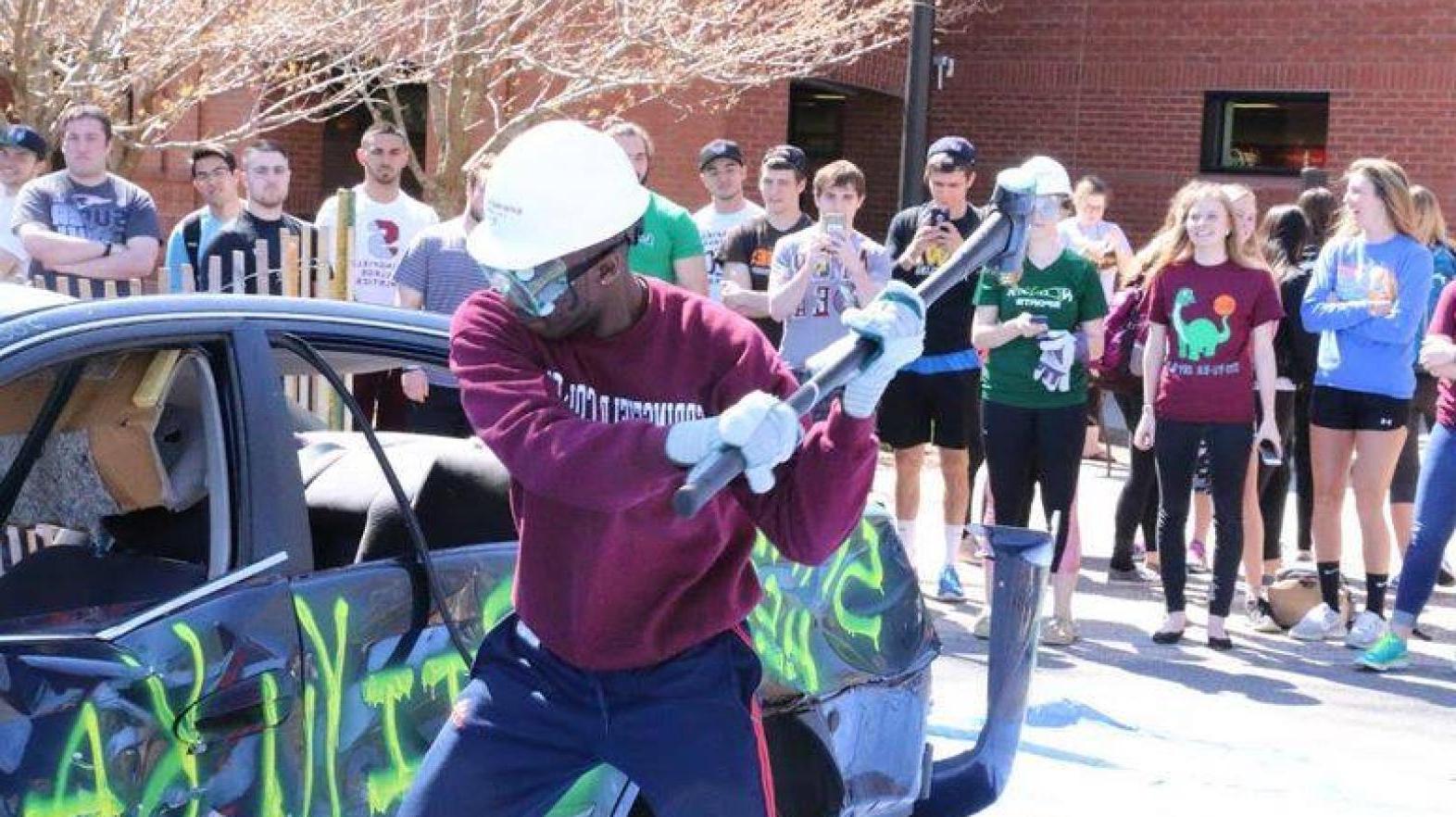 A student swings a hammer at a car as part of the whack-a-car event at Sti-Yu-Ka